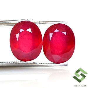 Puede incluir: Dos piedras preciosas rojas de forma ovalada con corte facetado. Las piedras preciosas están sujetas por unas pinzas.