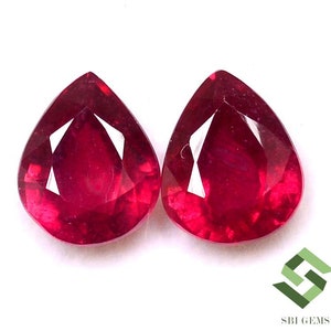 Puede incluir: Dos piedras preciosas de rubí en forma de pera, cada una con un color rojo intenso y un corte facetado.