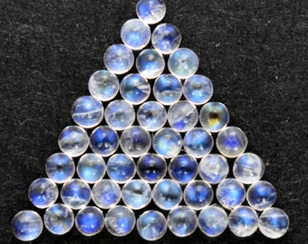 Puede incluir: Una disposición triangular de 28 cabujones redondos de piedra lunar iridiscente. Las piedras son de un blanco translúcido con un brillo azul.
