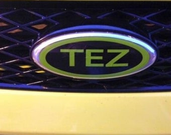 May include: A black and green oval emblem with the word "TEZ" in white letters on a yellow car.