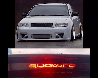 May include: A white Audi with a black grille and a red "quattro" emblem on the back. The car has a custom body kit and lowered suspension.