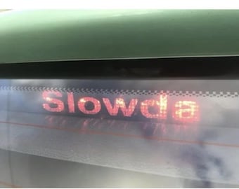 May include: A red and white checkered sticker on the back of a car with the word "Slowdown" written in red.