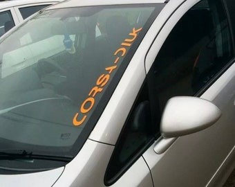 May include: A silver car with a black window and a black side mirror. The car has a sticker on the windshield that says "CORSA-D11K".