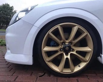 May include: A white car with a gold alloy wheel. The wheel has a multi-spoke design and a black center cap with a logo.