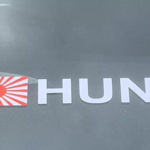 May include: A white sticker with the word "HUNT" in large, bold letters. A red and white Japanese flag is to the left of the word.