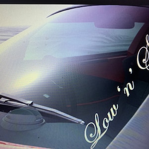 Peut inclure: Un autocollant en vinyle blanc avec le texte "Slow 'n' Slow" sur le pare-brise d'une voiture.