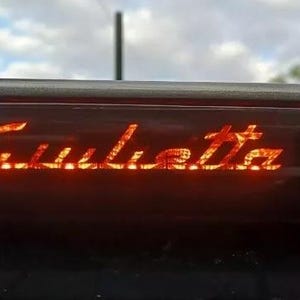 Può includere: Primo piano del lunotto posteriore di un'auto con la scritta "Giulietta" in lettere arancioni.
