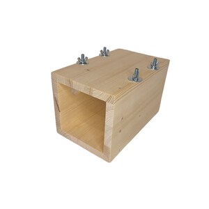 May include: A wooden box with a square opening, secured with four metal screws. The box is made of light-colored wood and has a natural finish.