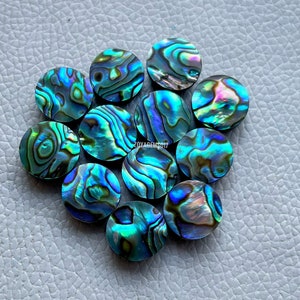 May include: A group of 10 round iridescent abalone shell cabochons. The cabochons are approximately 1 inch in diameter and have a variety of blue, green, and purple colors.