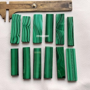 May include: A collection of rectangular malachite stones with varying patterns of dark and light green stripes. A brass measuring tool is in the background. The text "ZOYAGEMS017" is visible on the image.
