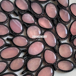 Puede incluir: Una colección de colgantes de cuarzo rosa con engarces de macramé negro. Los colgantes tienen varias formas ovaladas y de lágrima, cada uno con una piedra rosa pulida y translúcida. El texto "ZOYAGEMS017" es visible.