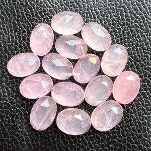Könnte beinhalten: Eine Sammlung von 15 ovalen, facettierten, rosafarbenen Rosenquarzsteinen. Die Steine sind durchscheinend und haben ein natürliches, wolkiges Aussehen.