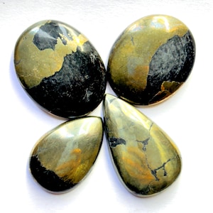 Pode incluir: Quatro pedras de pirita polidas em várias formas, dispostas para se assemelharem a uma borboleta. As pedras têm um esquema de cores metálico dourado e preto, com uma superfície refletora. A disposição está sobre um fundo branco.