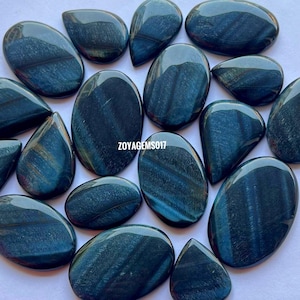 May include: A collection of 17 blue and green tiger's eye cabochons, each with a unique pattern of stripes. The stones are smooth and polished, and they have a slightly iridescent sheen.