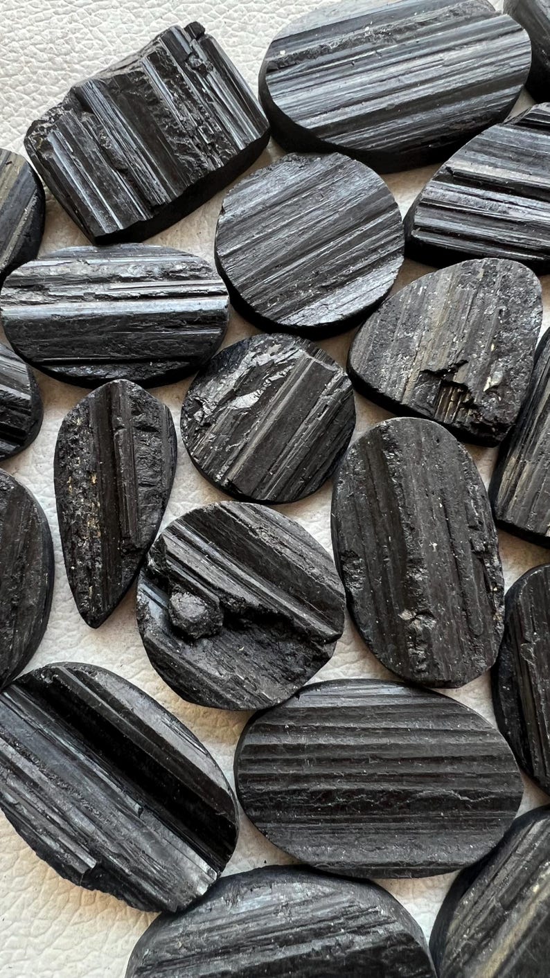 May include: A collection of black tourmaline stones, each with a unique shape and striated texture. The stones are arranged on a white surface.