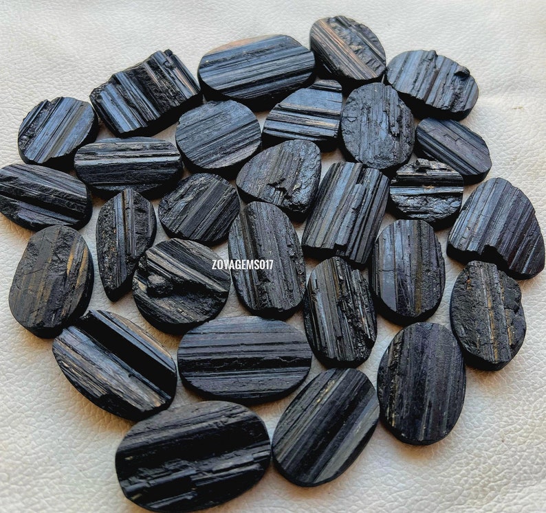 May include: A collection of black tourmaline stones, also known as schorl, with a striated, or striated, pattern. The stones are oval shaped and have a smooth, polished finish.