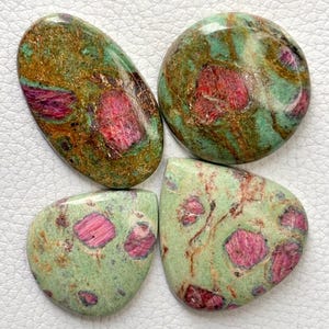 May include: Four polished cabochons of ruby in zoisite featuring a mix of vibrant magenta-pink ruby crystals embedded within a matrix of mottled light green, dark green, and earthy brown zoisite with a smooth, glossy, and reflective surface finish.