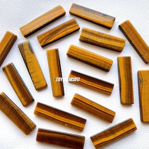 May include: A collection of 15 smooth, polished tiger's eye stones, each cut into a rectangular shape. The stones are a rich golden brown colour with a subtle shimmer.