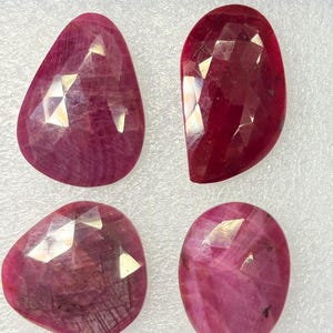 Puede incluir: Cuatro rubíes facetados en diversos tonos de rosa intenso y rojo. Cada piedra preciosa presenta una superficie pulida con facetas geométricas que reflejan la luz, mostrando inclusiones naturales y texturas dentro de las estructuras.