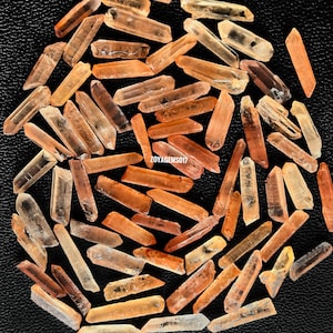 May include: A collection of approximately 50 small, raw, orange-brown quartz crystals. The crystals are pointed and have a natural, rough texture.