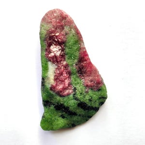 May include: A raw, irregularly shaped mineral specimen featuring a vibrant combination of deep magenta-red crystalline clusters embedded within a bright green matrix, accented by thin, dark black streaks running across the lower section.