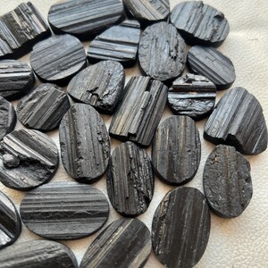 May include: A collection of black tourmaline gemstone cabochons, each with a unique striated pattern. The stones are oval shaped and have a smooth, polished finish.