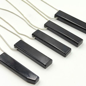 May include: Five necklaces featuring smooth, rectangular black pendants suspended from thin, silver-colored chains. Each pendant has a polished, glossy finish with rounded edges, arranged in a diagonal row against a plain white background.