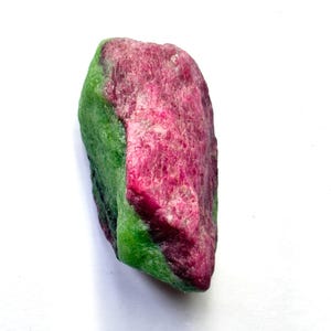 May include: A raw, unpolished mineral specimen featuring a distinct colour contrast between a vibrant, deep magenta-pink section and a textured, bright green section. The stone has an irregular, elongated shape with visible crystalline facets.