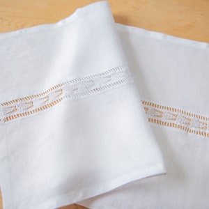 May include: White linen table runner with delicate white lace trim. The lace trim features a repeating pattern of small, rounded shapes.