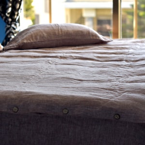 May include: A gray linen duvet cover with button closures. The duvet cover is on a bed with a pillow and a brown blanket.
