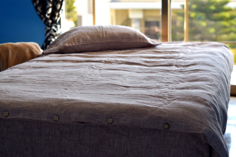 May include: A gray linen duvet cover with button closures. The duvet cover is on a bed with a pillow and a brown blanket.