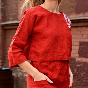 May include: A red linen dress with white embroidered snowflakes. The dress has a cropped top and a skirt with pockets.