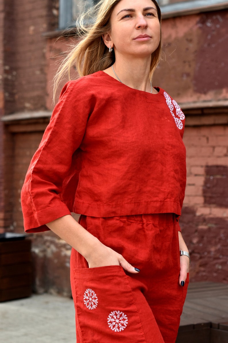 May include: A red linen dress with white embroidered snowflakes. The dress has a cropped top and a skirt with pockets.
