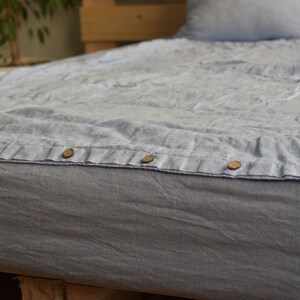 May include: A light blue linen duvet cover with wooden buttons. The duvet cover is on a bed with a wooden headboard.