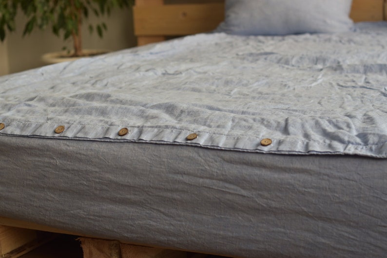 May include: A light blue linen duvet cover with wooden buttons. The duvet cover is on a bed with a wooden headboard.