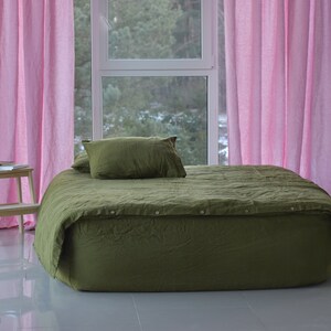 May include: A green linen duvet cover with button closures on a bed with pink curtains in a bedroom.