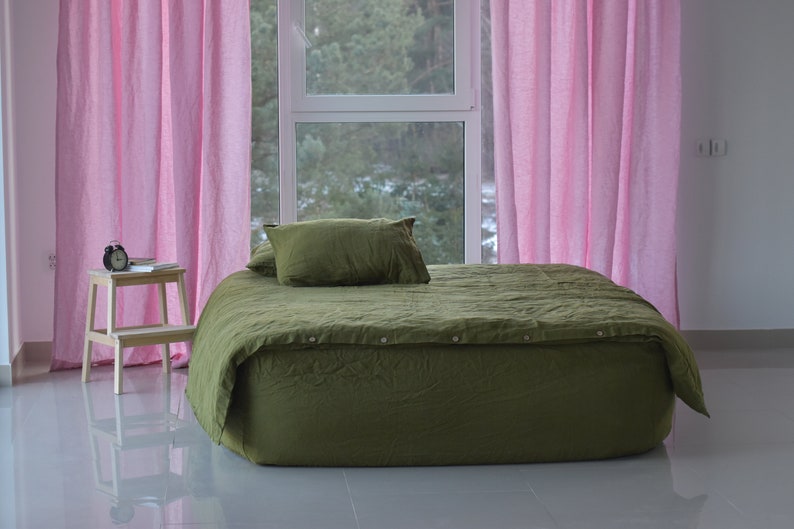 May include: A green linen duvet cover with button closures on a bed with pink curtains in a bedroom.