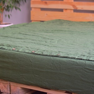 May include: A dark green linen fitted sheet with button closures. The sheet is on a wooden pallet.