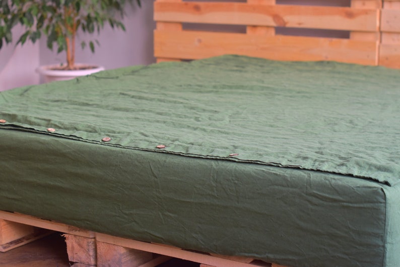 May include: A dark green linen fitted sheet with button closures. The sheet is on a wooden pallet.