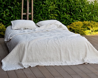 Puede incluir: Una manta de tiro de lino a rayas blancas y grises está doblada en una cama con dos fundas de almohada a juego. La cama está en una plataforma de madera.