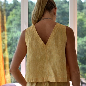 May include: A sleeveless yellow linen top with a deep V-neckline. The top is made of a lightweight, breathable fabric and has a relaxed fit.