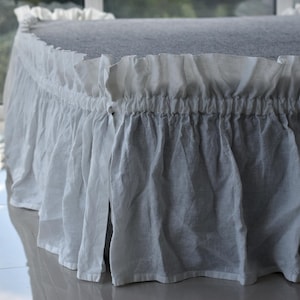 Puede incluir: Falda de cama de lino blanco con un borde con volantes. La falda está fruncida en la parte superior y tiene un diseño sencillo.