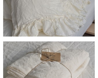 Puede incluir: Una pila de fundas de almohada de lino blanco con un borde con volantes, atadas con una cuerda y una etiqueta marrón que dice "100% Lino, Hecho en Francia".