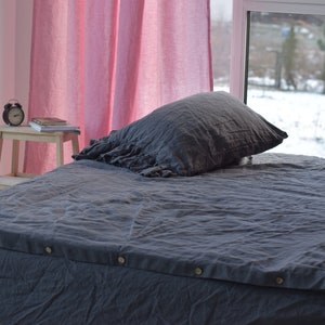 May include: A gray linen duvet cover with a ruffled pillow on a bed. The bed is in a room with pink curtains and a window overlooking a snowy backyard.