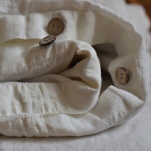 May include: White linen fabric folded with three wooden buttons. The fabric is soft and textured.
