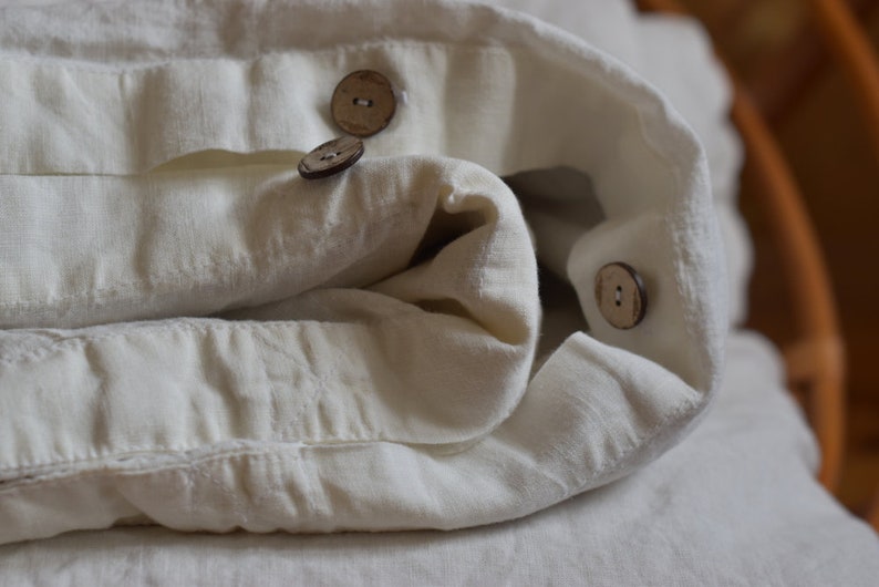 May include: White linen fabric folded with three wooden buttons. The fabric is soft and textured.
