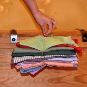 May include: A stack of fabric swatches in various colours and patterns, including green, red, brown, and beige. The swatches are folded and arranged in a pyramid shape.