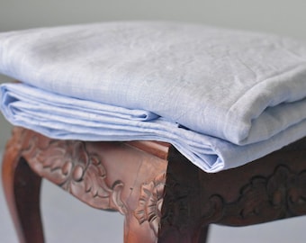 Puede incluir: Una tela de lino azul claro doblada sobre una mesa de madera con tallas intrincadas.