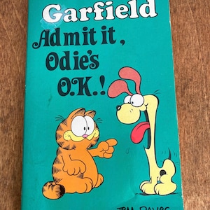 May include: A vintage Garfield comic book with a teal cover. The title reads "Garfield Admit it, Odie's O.K.!" Garfield, an orange cat, points at Odie, a yellow dog with a long tongue. The book is a selected collection of Garfield cartoons by Jim Davis.