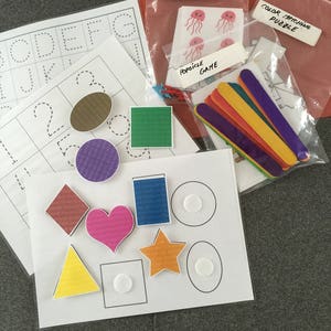 May include: A set of educational toys for children, including a counting game with jellyfish stickers, a color matching puzzle, a popsicle stick game, and a set of shape and number tracing worksheets.